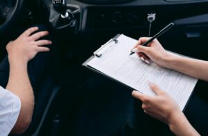 Close-up of a person writing on a clipboard inside a car, showing hands and a gear shift.